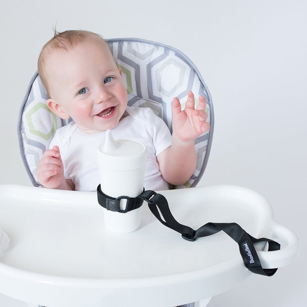 Toddler using BooginHead SippiGrip in black to keep the sippy cup clean and attached to their highchair. Adjustable strap can attach to bottles, sippy cups or toys. Essential baby and toddler supply! Easy to clean. 