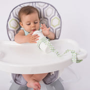 Toddler using BooginHead SippiGrip in Delicate Dot Green to keep the sippy cup clean and attached to their highchair. Size adjustable strap can attach to bottles, sippy cups or toys. Essential baby and toddler supply! Easy to clean. 